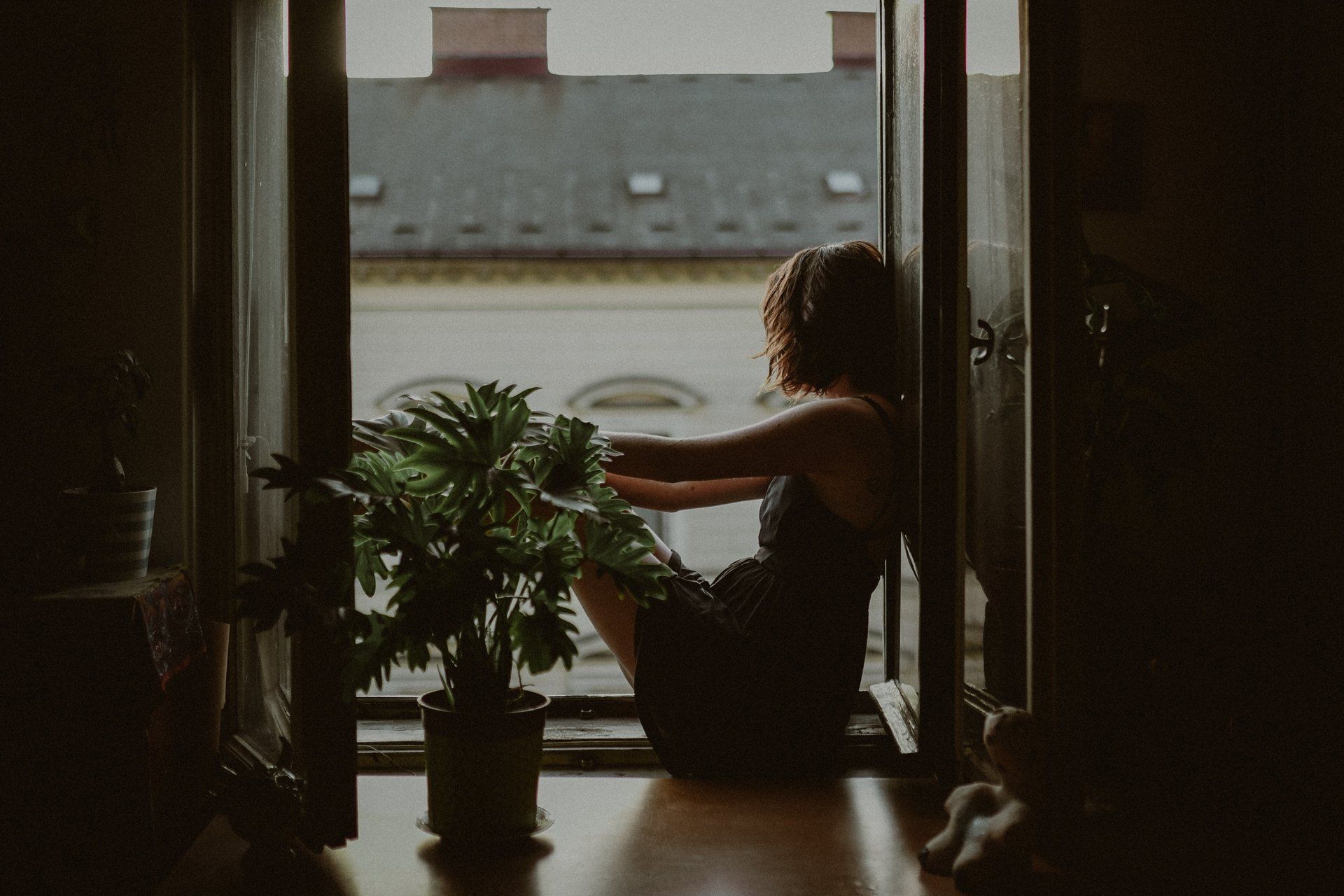 A woman is sitting on the floor in front of a window looking out.