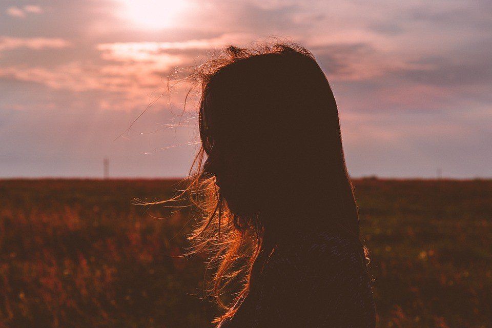 A silhouette of a woman standing in a field at sunset.