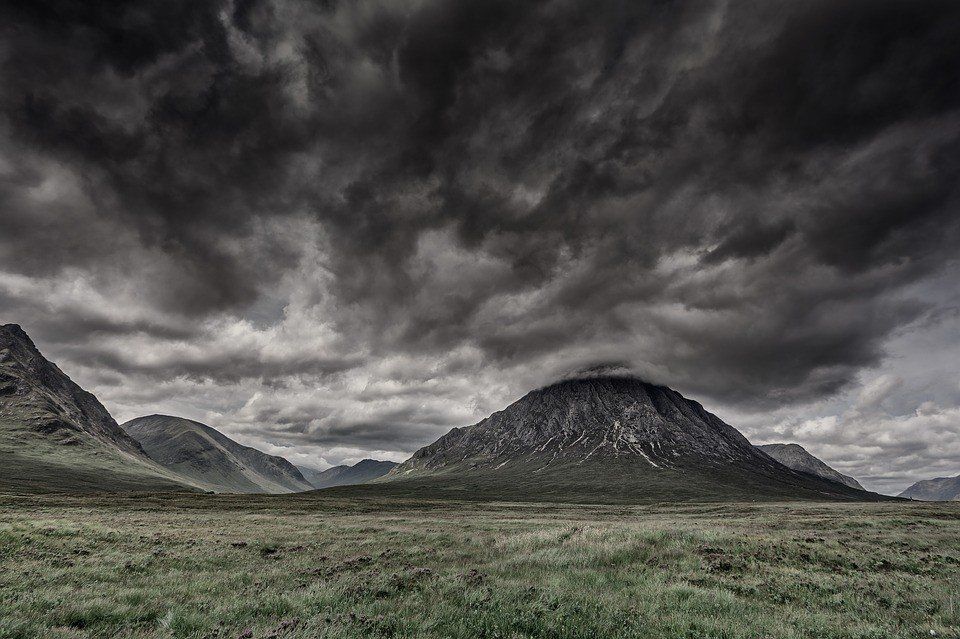 A black and white photo of a mountain range with a cloudy sky in the background.