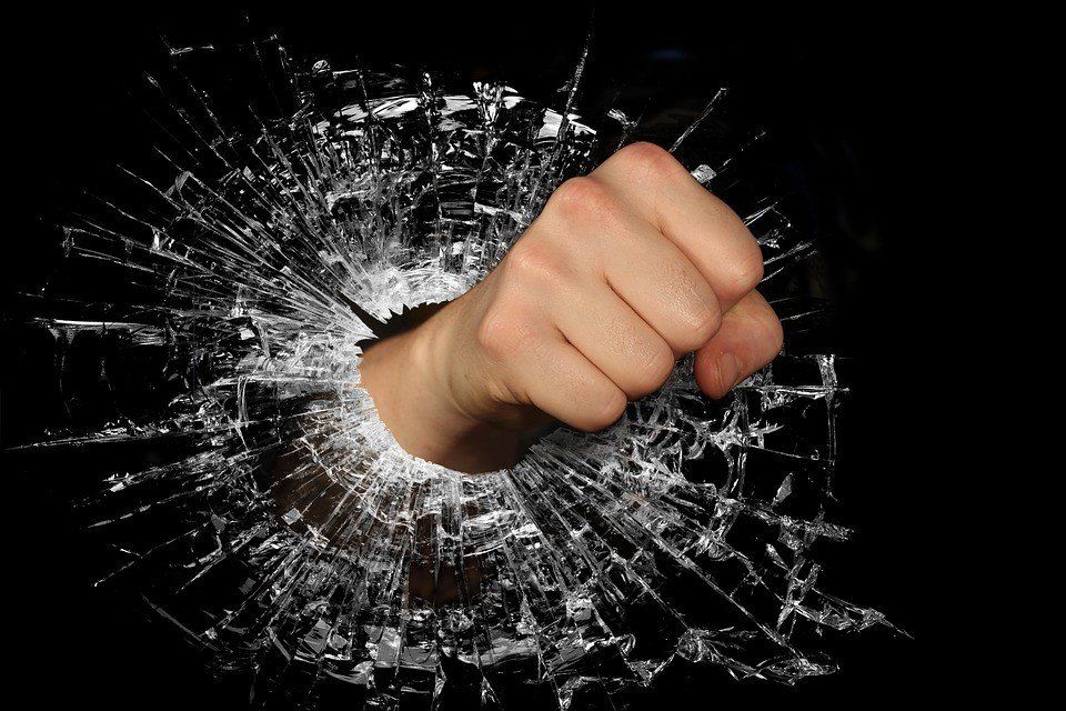 A fist is breaking through a broken glass wall.