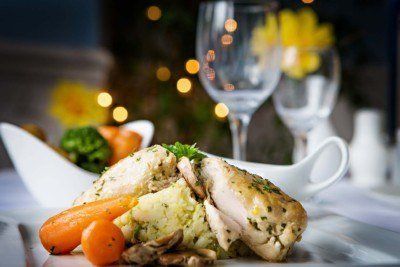 Chicken and risotto dish with vegetables, wine glasses, and soft background lights.
