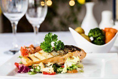 Grilled salmon fillet on mixed greens, with a side of vegetables and water glasses in a restaurant setting.