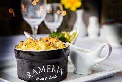 Macaroni and cheese in a ramekin on a white tray, with a side of greens and a gravy boat. Elegant restaurant setting.