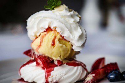 Pavlova dessert: meringue base, ice cream scoop, whipped cream, strawberry sauce, garnished with berries and mint.