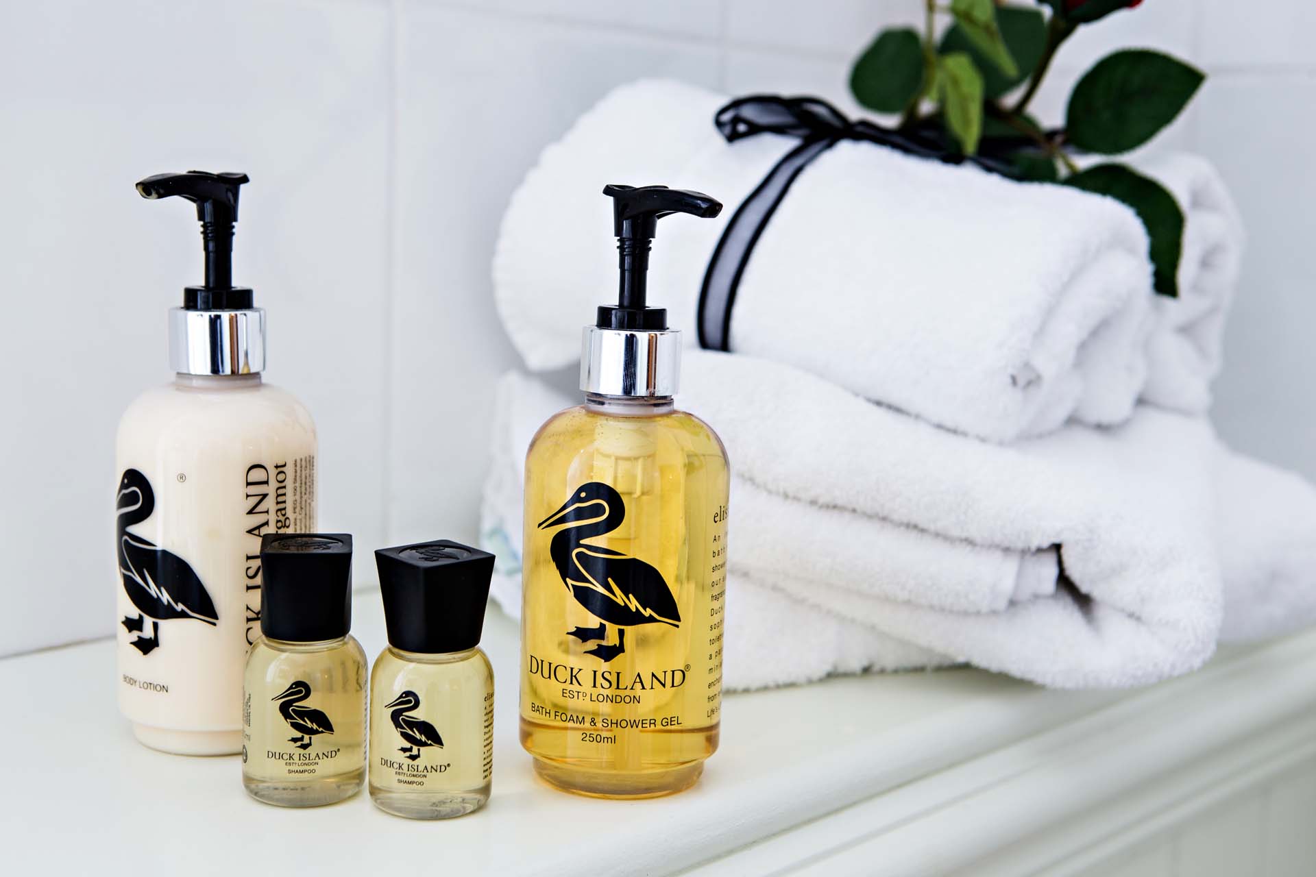Bottles of bath products with a pelican logo next to rolled white towels on a shelf.