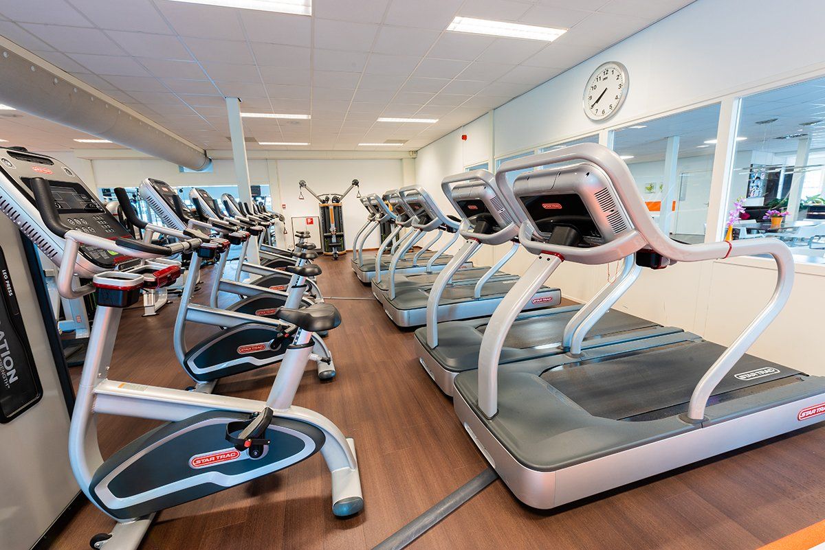 Een rij loopbanden in een sportschool met een klok aan de muur.