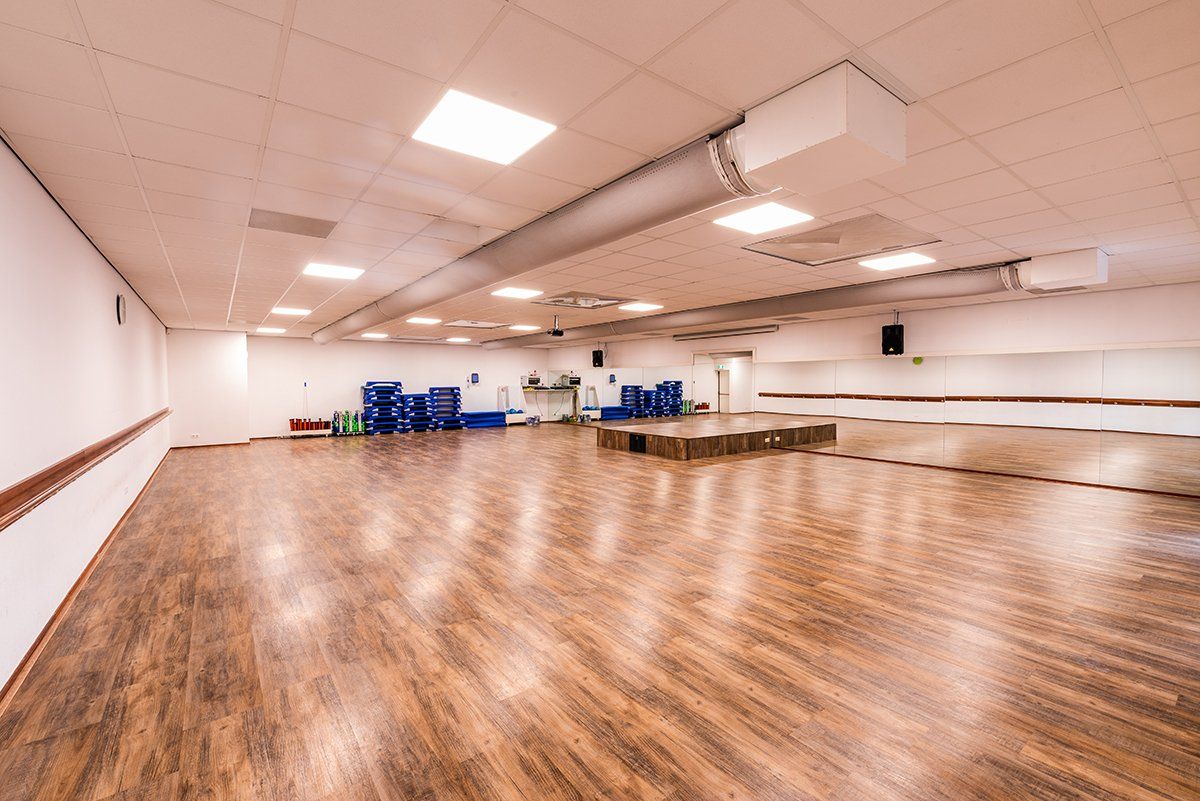 Een lege dansstudio met houten vloeren en een grote spiegel.