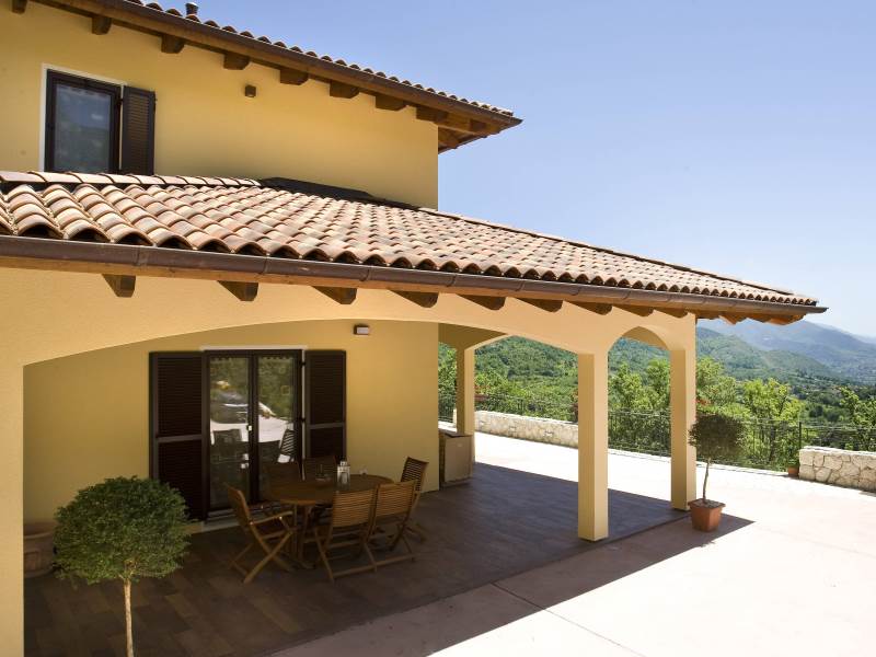 Una casa gialla con il tetto di tegole e un tavolo e delle sedie sulla veranda