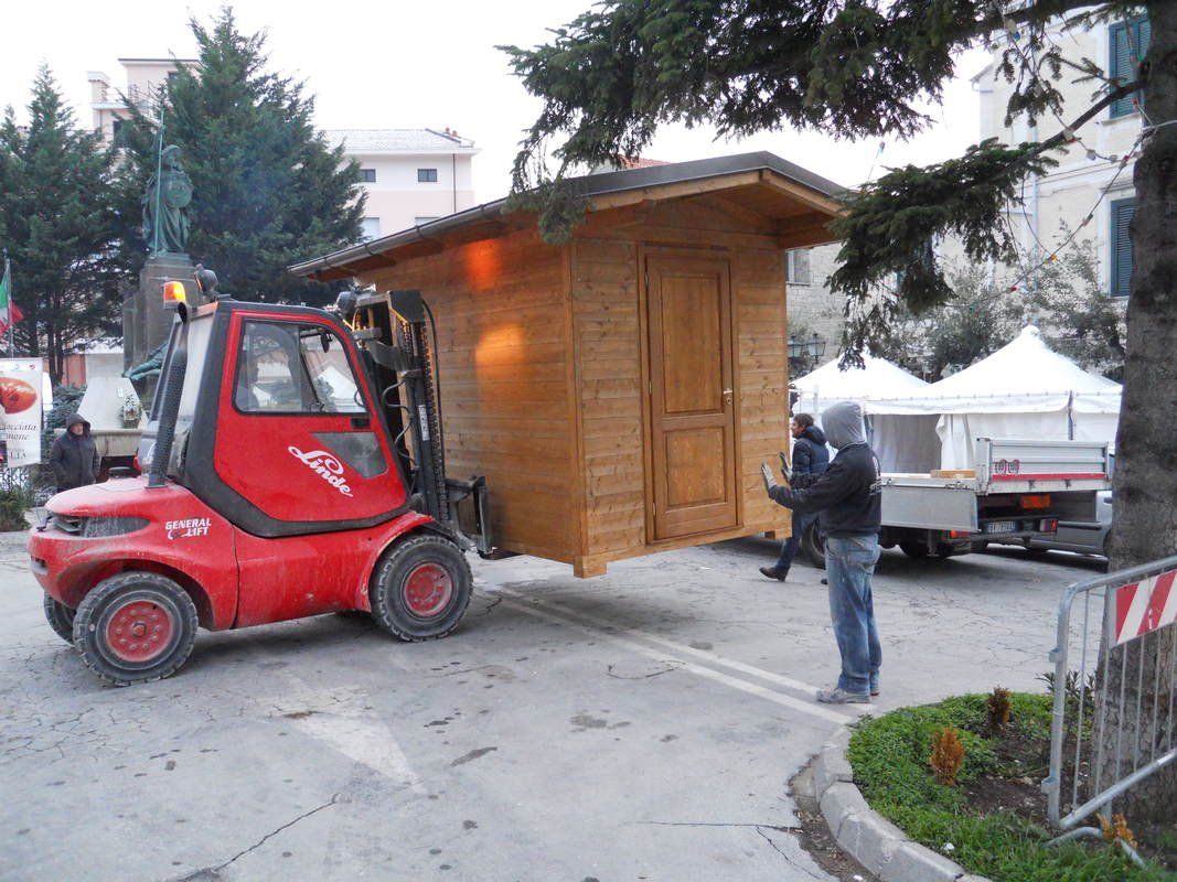 Un carrello elevatore rosso trasporta un piccolo edificio di legno