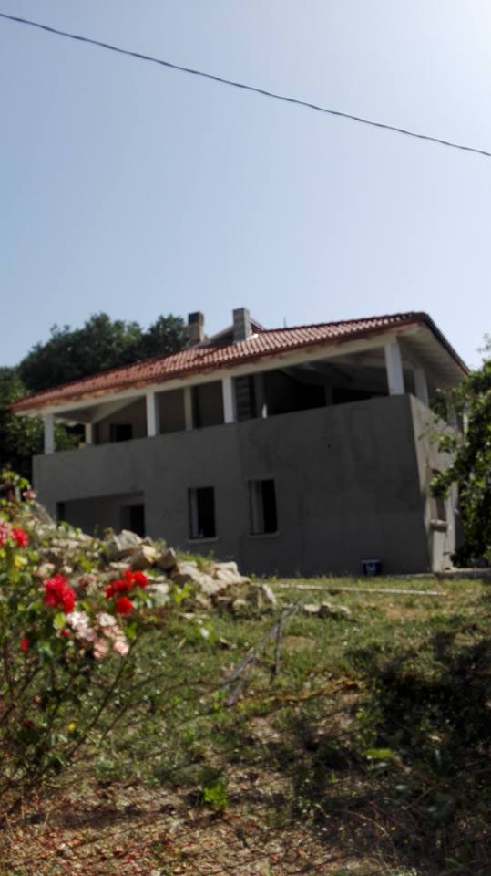 Una grande casa con il tetto di tegole rosse si trova in cima a una collina erbosa.
