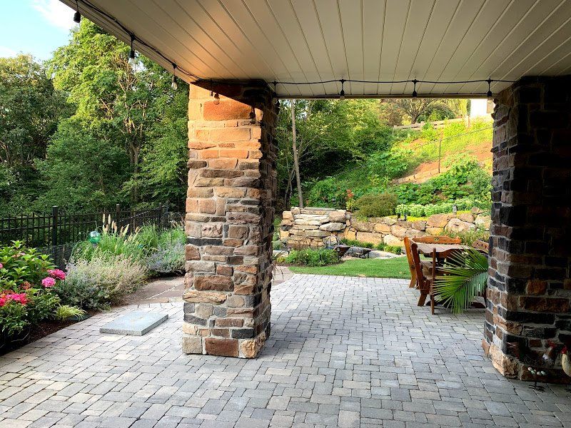 A stone patio with a table and chairs under a covered patio.
