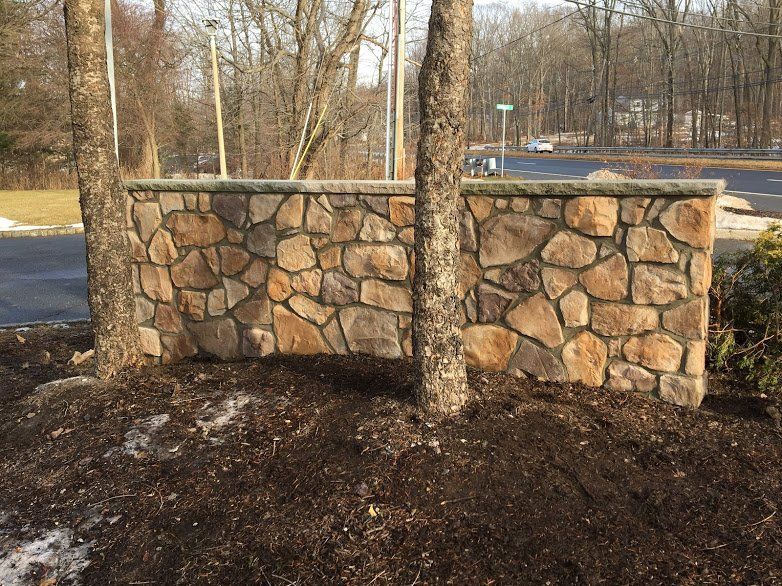 A stone wall is surrounded by trees and a pile of mulch.