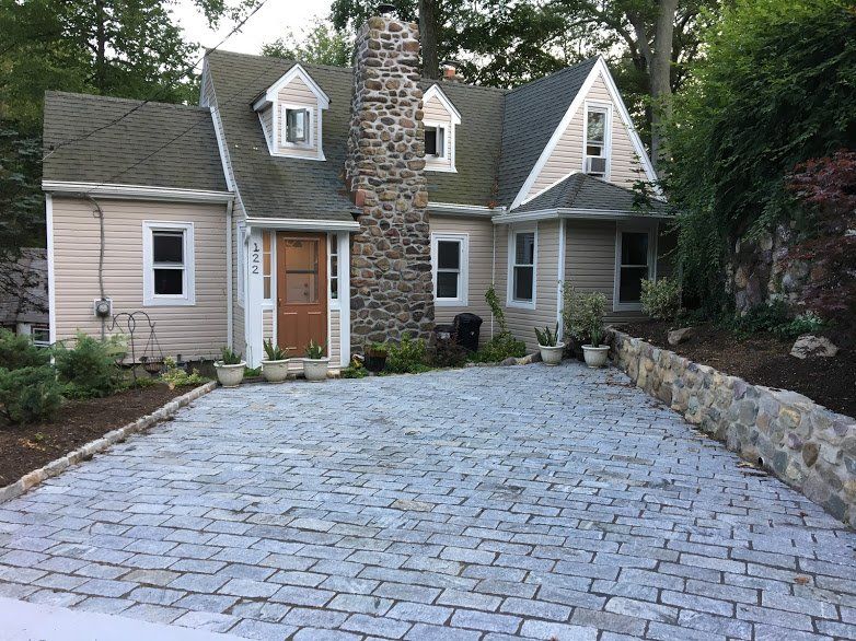 A house with a stone chimney and a brick driveway in front of it.