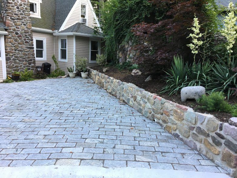 A brick driveway leading to a house with a stone wall.