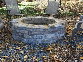 A fire pit is surrounded by leaves and chairs.