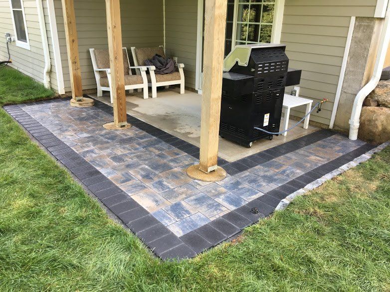 A patio with a grill and chairs under a covered porch.