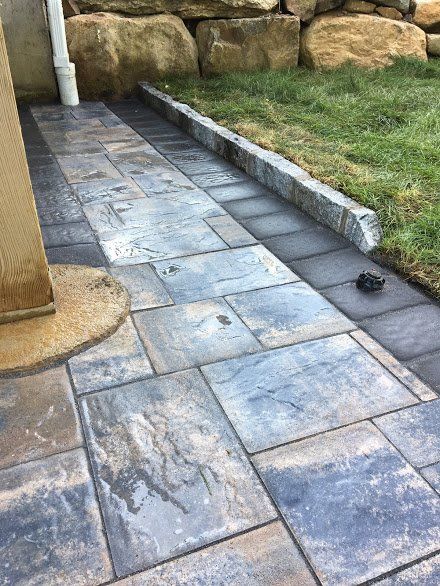 A brick walkway leading to a lawn with rocks in the background.