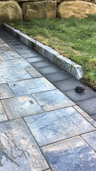 A stone walkway leading to a grassy area with rocks in the background.