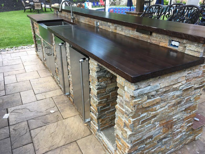 An outdoor kitchen with a wooden counter top and a stainless steel sink.