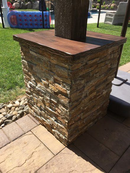 A stone pillar with a wooden top is sitting on a patio next to a pool.