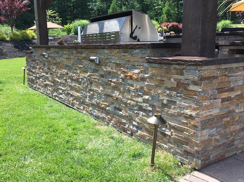A stone wall with a grill on top of it in a backyard.