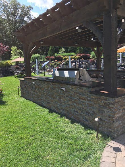 An outdoor kitchen with a grill under a pergola in a backyard.