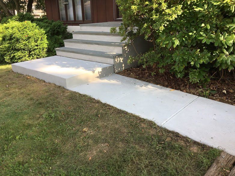 A concrete walkway leading to a set of stairs in front of a house.