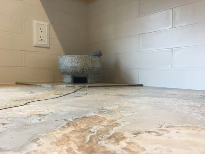 A mortar and pestle is sitting on a tiled floor in a kitchen.