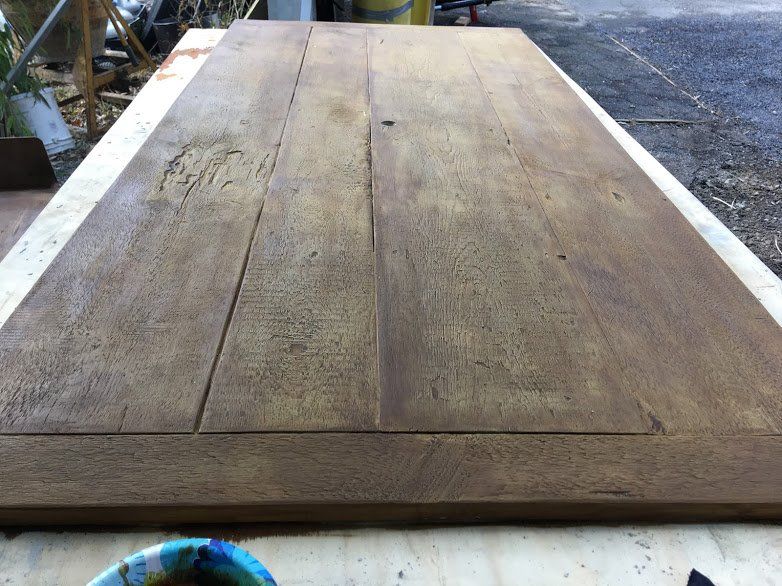 A large piece of wood is sitting on a table next to a bowl of paint.