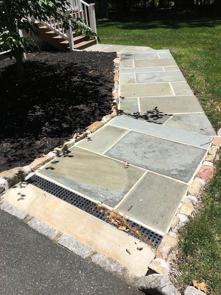 A stone walkway with a drain on the side of it