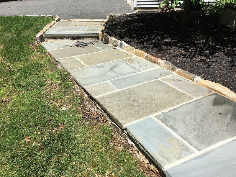A stone walkway is being built in the grass next to a driveway.
