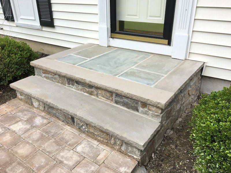 A stone porch with steps leading to the front door of a house.