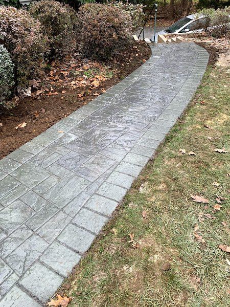 A concrete walkway leading to a driveway in a yard.