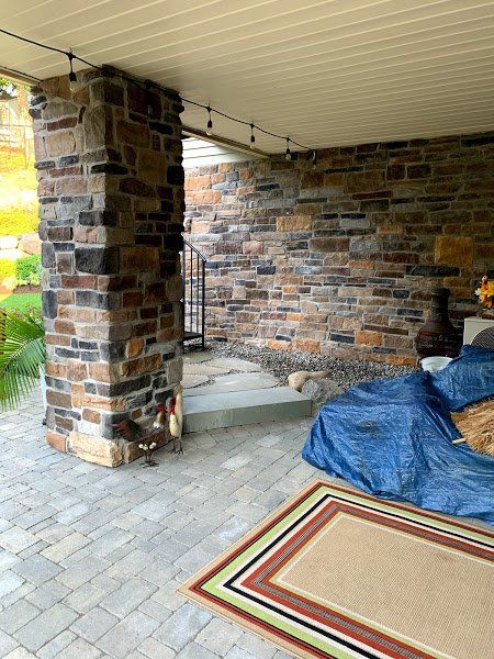 A dog is sitting on a rug on a patio next to a stone wall.