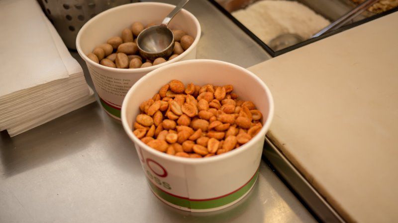 Two cups of peanuts, one raw, one roasted. A scoop rests in the raw peanuts.