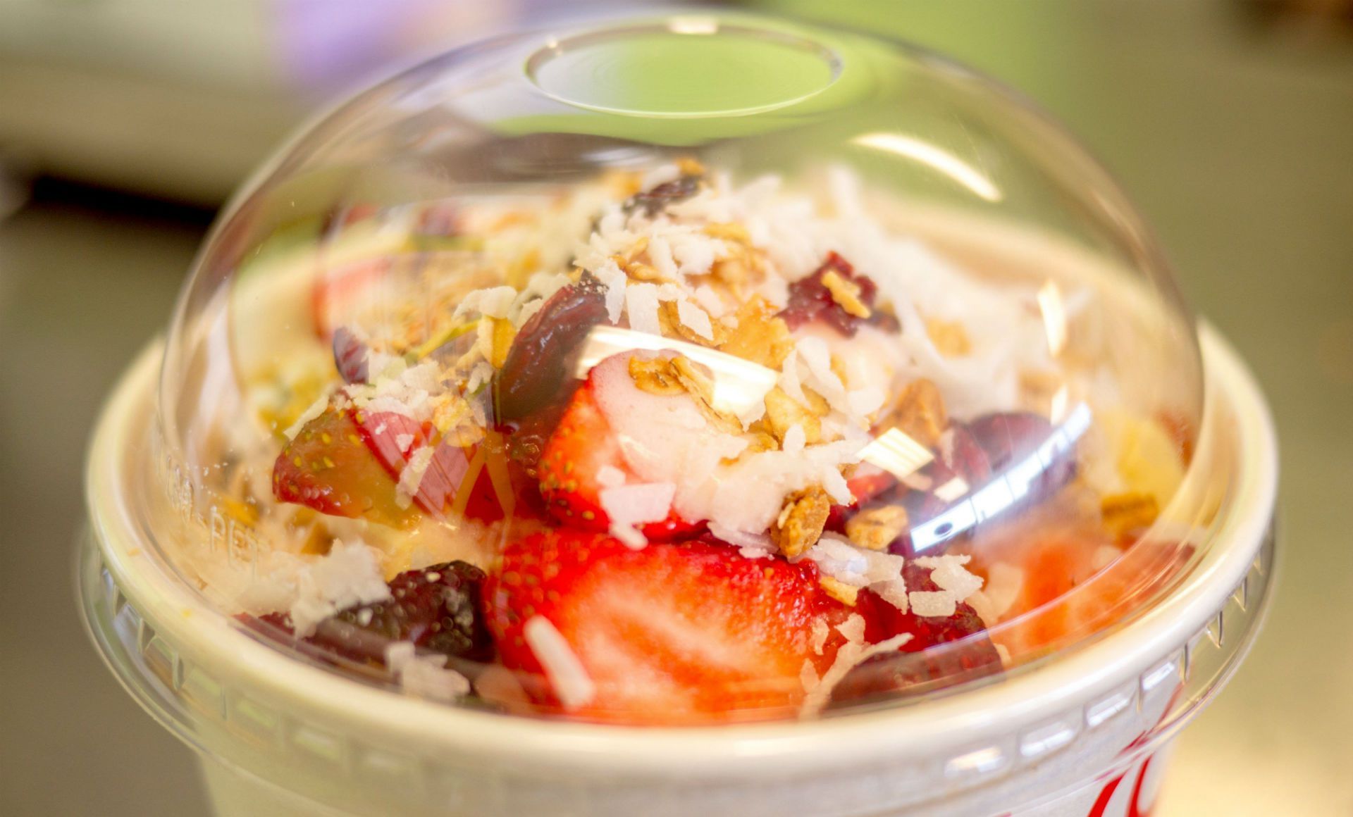 Acai bowl in clear plastic cup; topped with strawberries, coconut flakes, and granola.