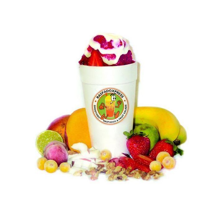 Cup of shaved ice with fruit toppings, surrounded by fruit.