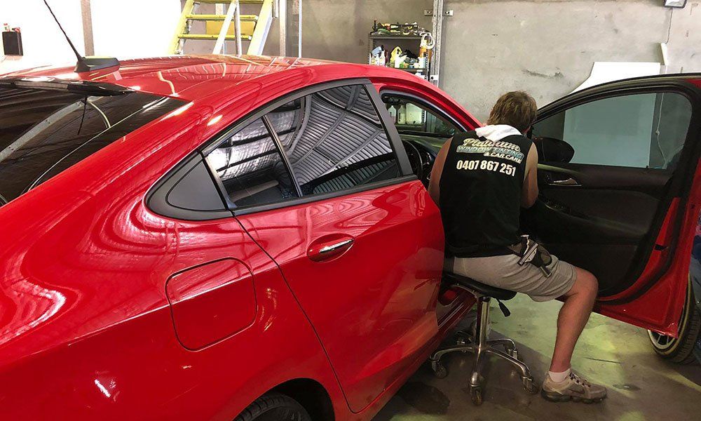 A man is sitting in a chair in front of a red car.