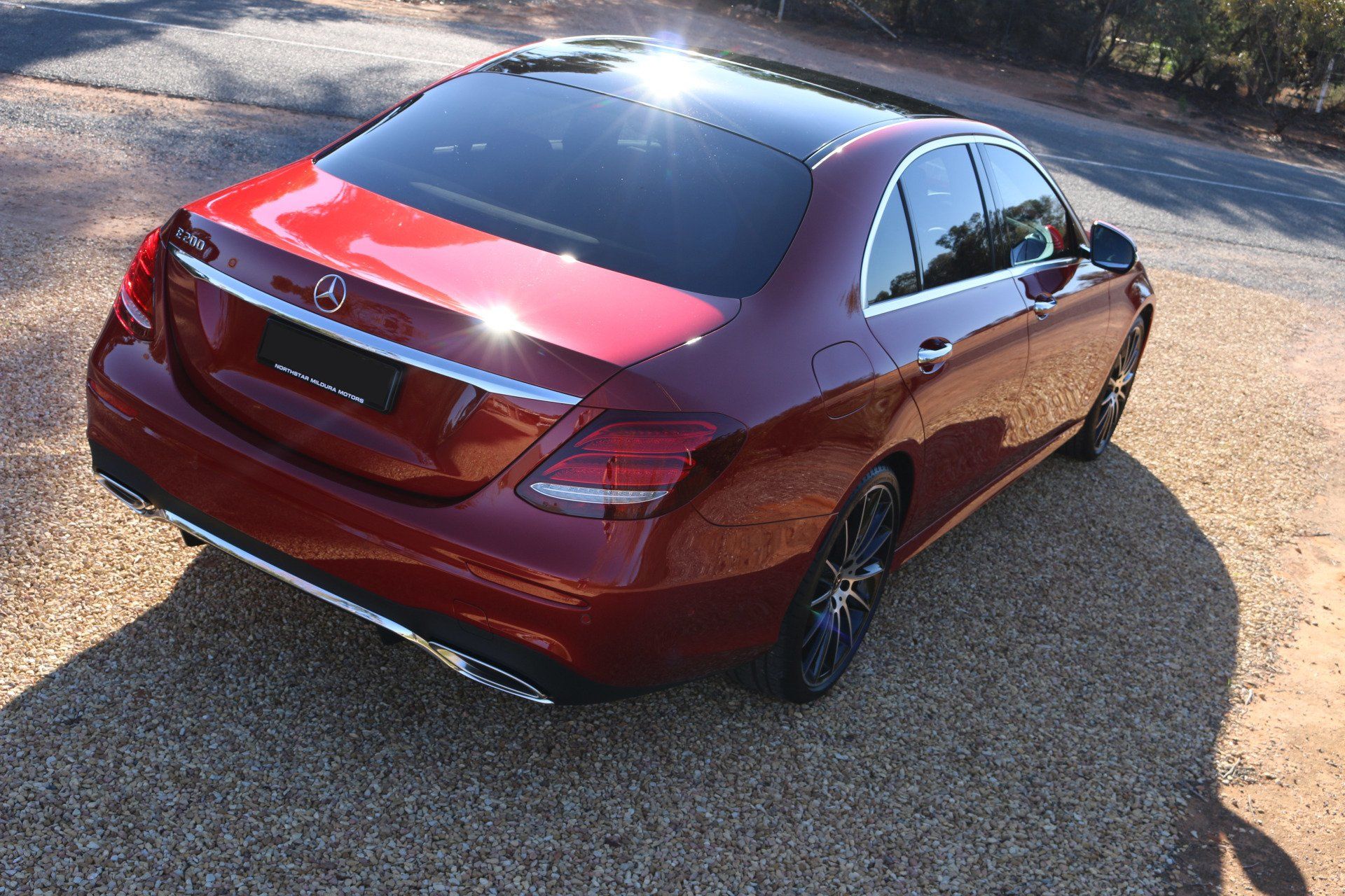 A red mercedes benz is parked on a gravel road
