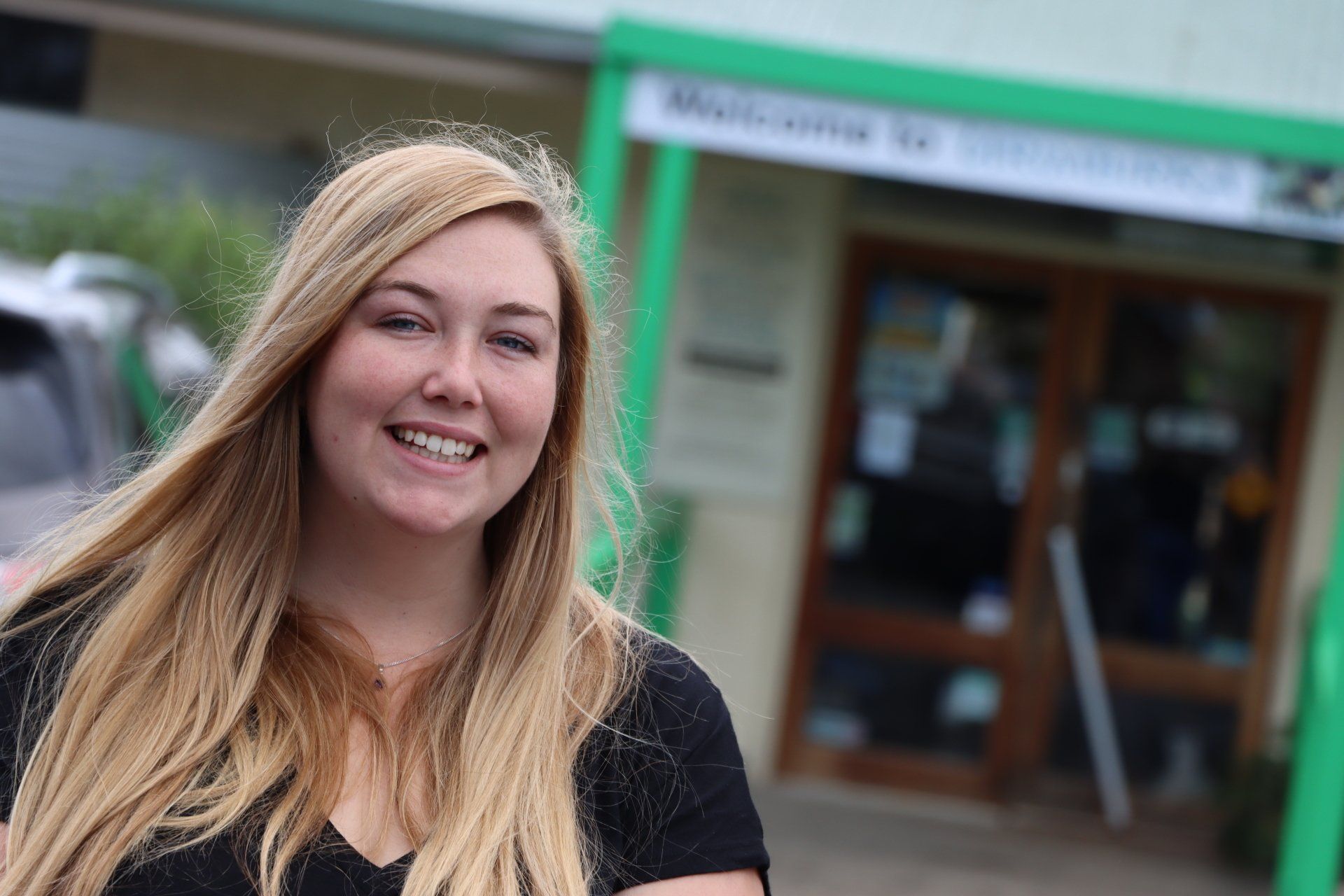 A woman with long blonde hair is smiling in front of a building.
