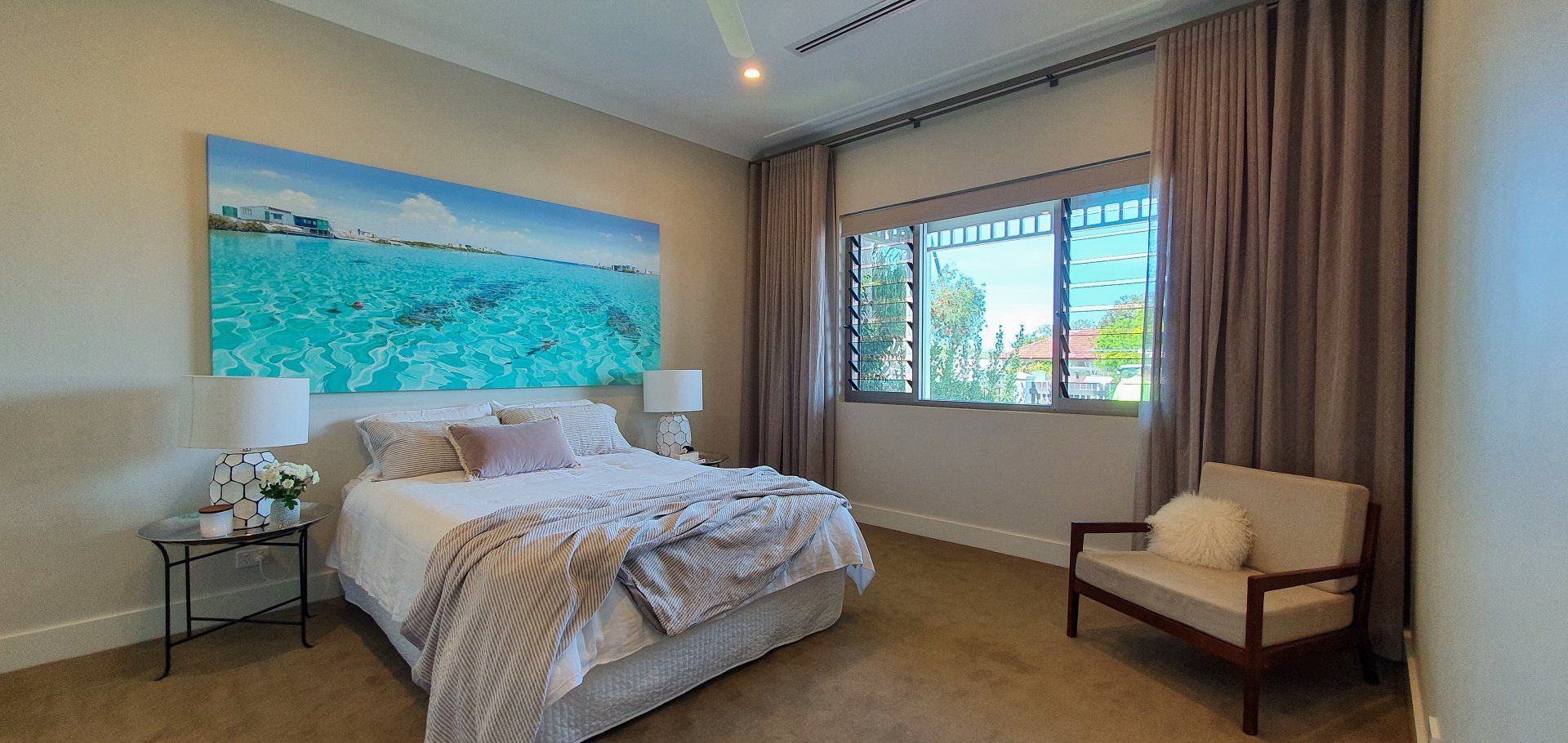 Bedroom with bed, ocean artwork, window with curtains, and armchair.