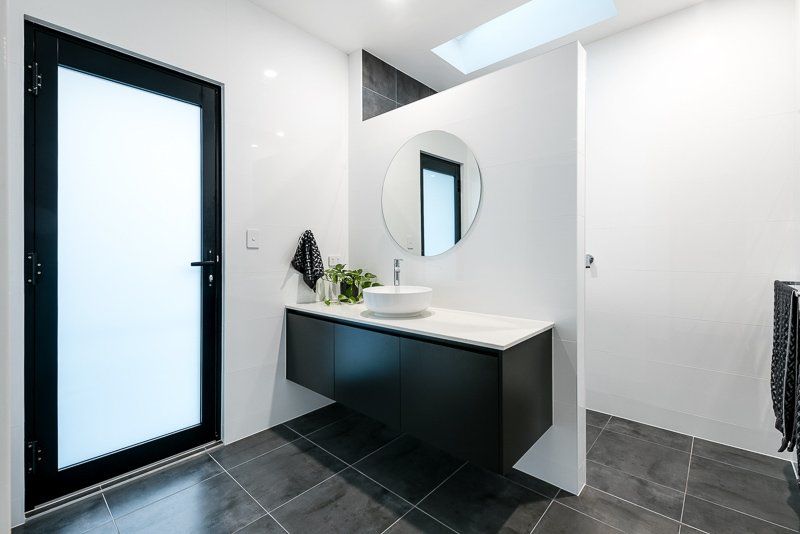 Modern bathroom with a black floating vanity, round mirror, and a frosted door.