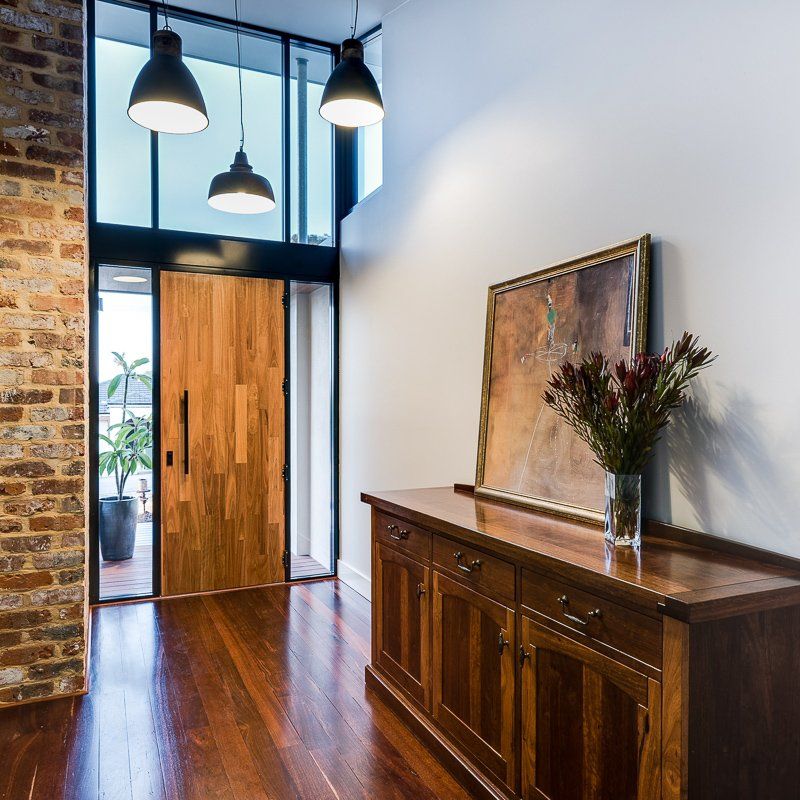 Entryway with wooden door, brick wall, dark wood cabinet, painting, and pendant lights.