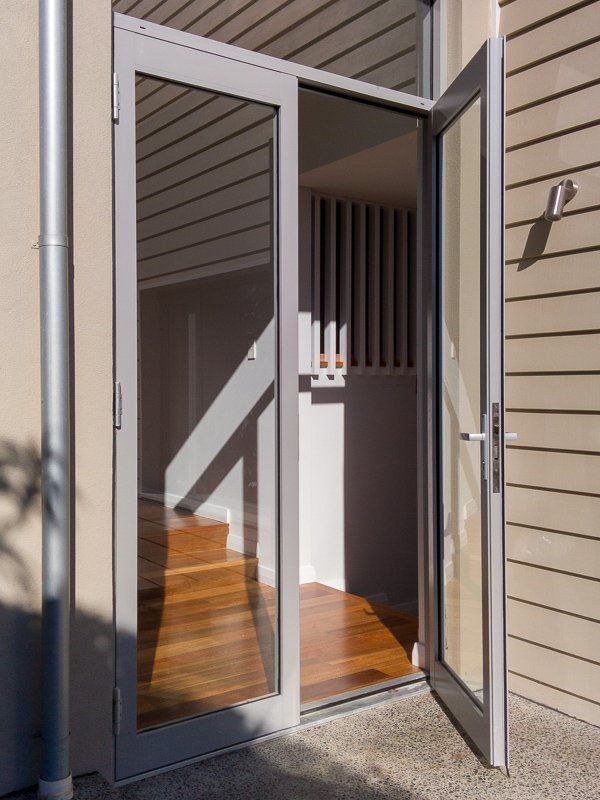 Glass door, one panel open, revealing wooden stairs and interior. Light gray frame, outdoor setting.