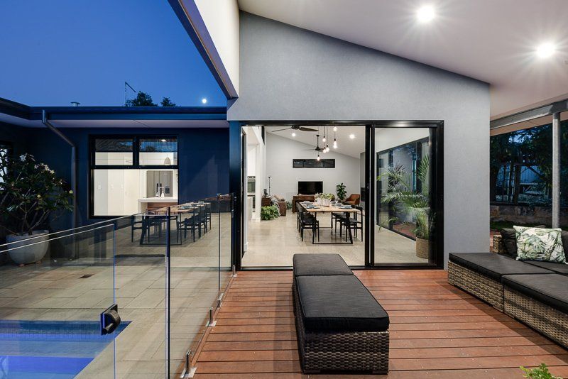 Modern home exterior with pool and open interior, featuring outdoor seating.