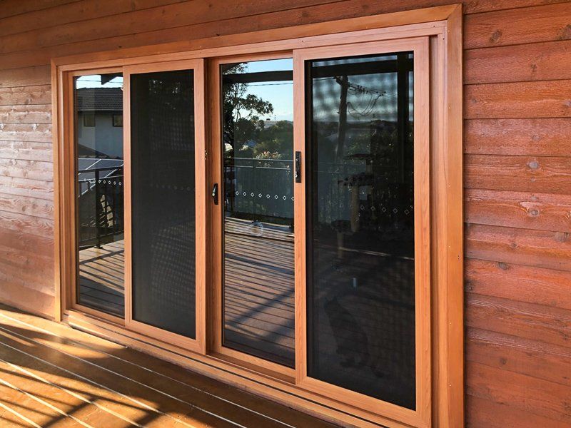 Sliding glass doors with brown frames and screens, set in a wood-paneled wall and deck.