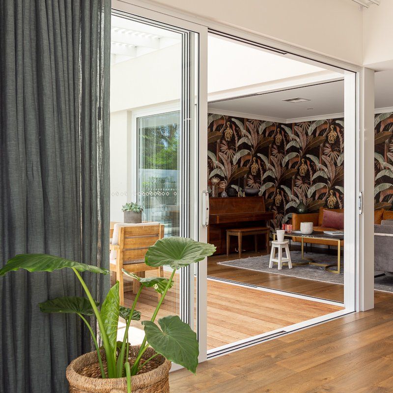 Sliding glass doors open to a living room with patterned wallpaper, a piano, and a sofa. A potted plant is in the foreground.