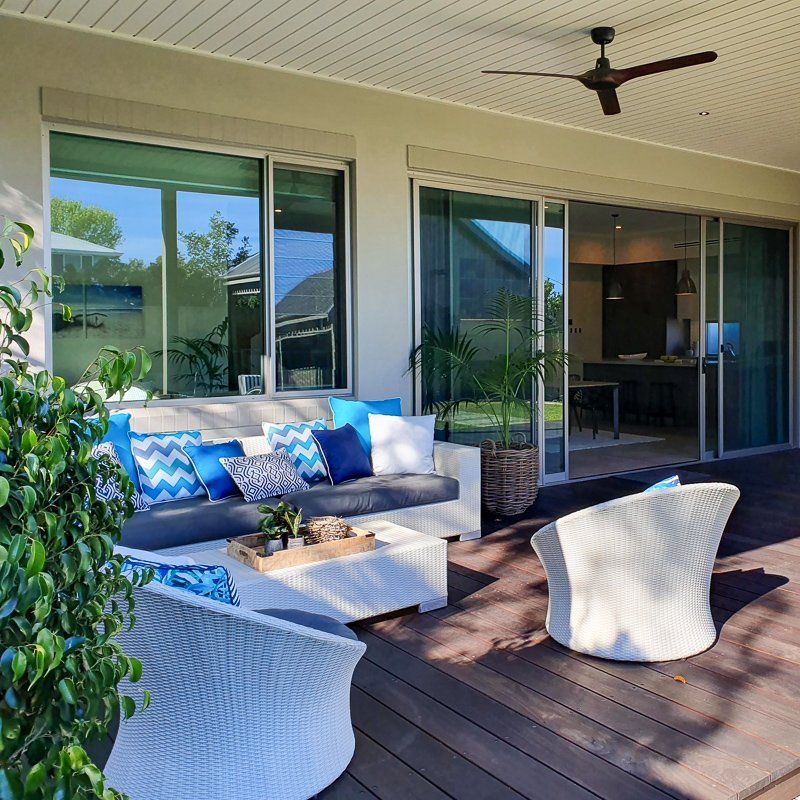Patio with white wicker furniture, blue pillows, and open sliding doors, sunny day.