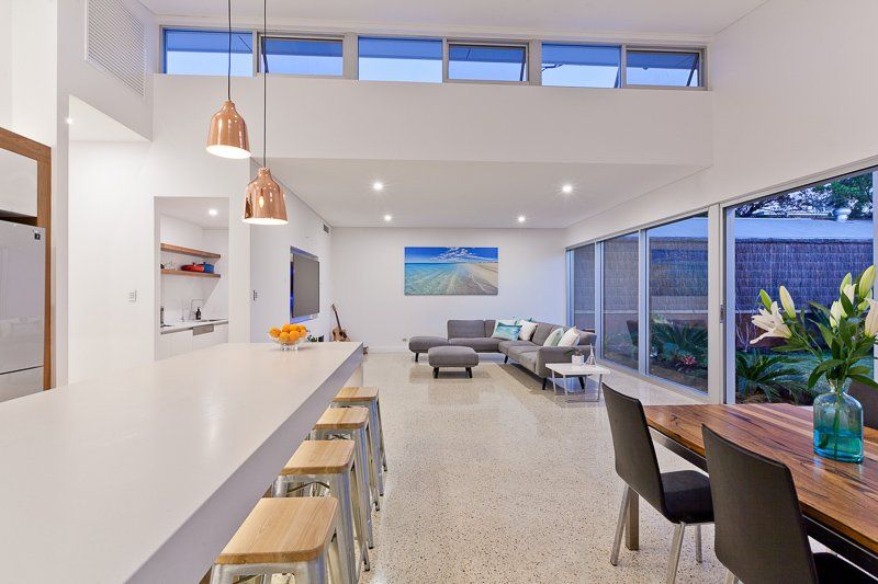 Spacious living area with modern furnishings: kitchen island with stools, sofa, dining table, and large windows.