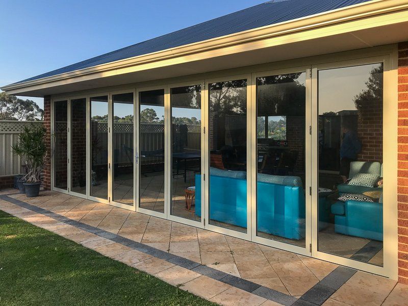 Exterior view of a house with beige framed folding glass doors, brick facade, and a stone patio.